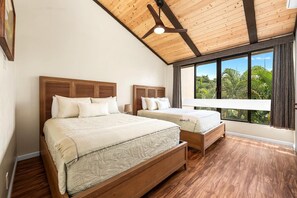 A bedroom with two beds, wooden headboards, a large window with a view of greenery, and a ceiling fan. - Kksr#4303 Direct Oceanfront, Top Floor, Ac! (Kailua-Kona)