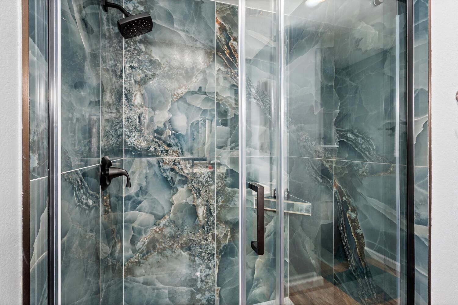 Eine gläserne Dusche mit einem marmorähnlichen Fliesenmuster.