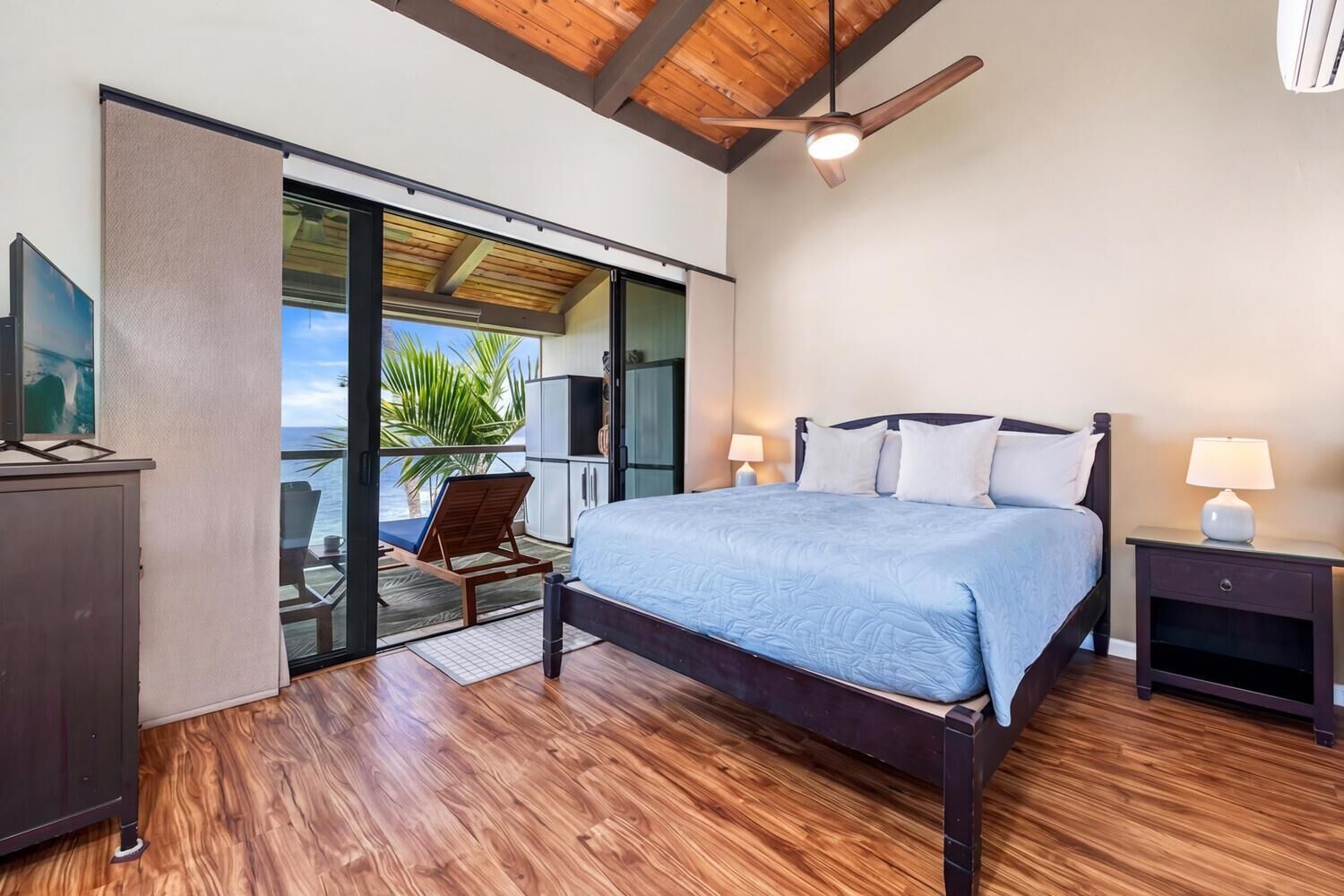 A bedroom with a bed, nightstands, a ceiling fan, and a view of the ocean.