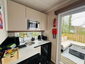 A compact kitchenette with a microwave, sink, and toaster, a fire extinguisher, and a sliding glass door to a patio with outdoor furniture. - Ravenswood Pod near Fort William (Fort William)
