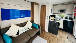 En kompakt opholdsstue med sofa, tekøkken og en dør til et andet rum.