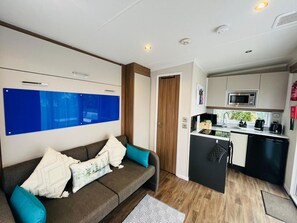 A compact living space with a sofa, a kitchenette, and a door leading to another room. - Ravenswood Pod near Fort William (Fort William)