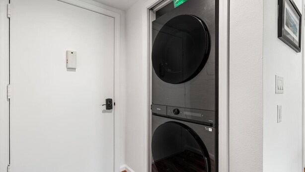 A laundry room with two stacked washers and dryers, a white door, and a wooden floor. - Kona Pacific E629: Beautifully Remodeled Condo! (Kailua-Kona)