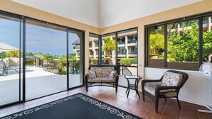A balcony with a view of a pool and buildings, furnished with wicker chairs and a small table. - Kona Pacific E629: Beautifully Remodeled Condo! (Kailua-Kona)