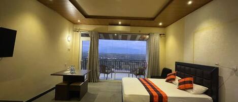 A hotel room with a bed, a desk, and a view through a large window.