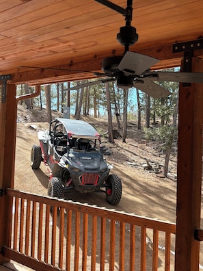 A wooden deck with a view of a forested area and a Polaris ROKO ATV parked on a dirt path. - Terrific 2-bedroom country house in charming Woodland Park (Woodland Park)
