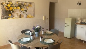 A dining area with a round table set for four, a kitchen with a refrigerator and a sink, and a painting of lemons on the wall. - Oasi del Silenzio Apartment in Relais with panoramic SPA (Piea)