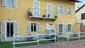 A yellow building with white shutters, a balcony with a railing, and a paved area with benches. - Oasi del Silenzio Apartment in Relais with panoramic SPA (Piea)