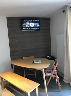 Ein Zimmer mit einem Holzesstisch, einer Bank, einem an der Wand montierten Fernseher und einem Stuhl.