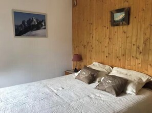 Ein Schlafzimmer mit Holz-Kopfteil, einem Bett mit weißer Bettwäsche, zwei Kissen, einem Nachttisch mit Lampe und einem gerahmten Bild an der Wand.