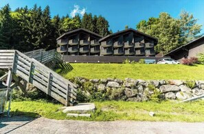Ein Chalet-Hotel mit mehreren Balkonen, einer Holztreppe und einer Steinstützmauer.