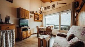 Un salon chaleureux avec un canapé, un téléviseur, des meubles en bois, une table à manger et un balcon offrant une belle vue.
