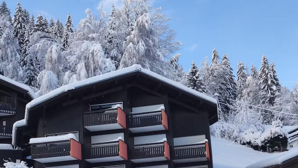 Un chalet enneigé doté de plusieurs balcons, entouré d’arbres.