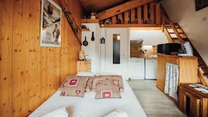 L'intérieur d'une cabane en bois, avec un lit, une cuisine et un escalier.