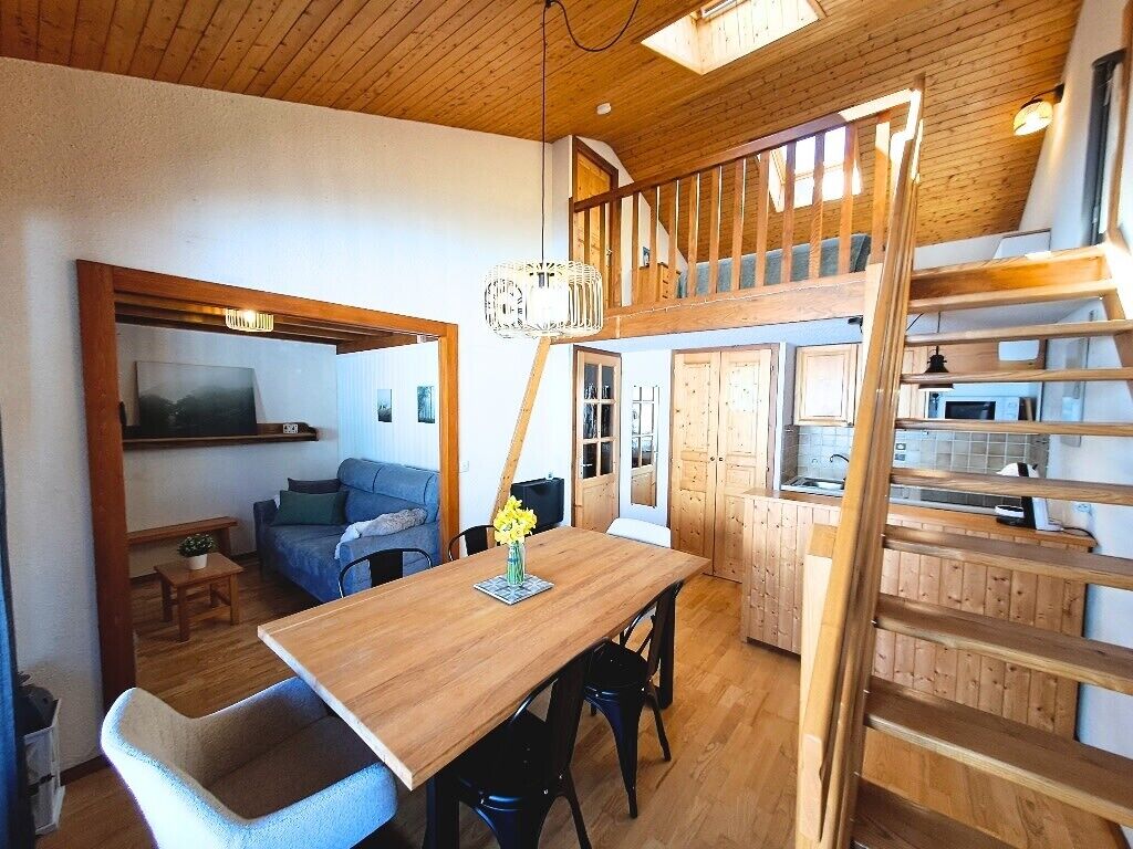 A loft-style room with a wooden dining table, a sofa, and a staircase leading to an upper level.