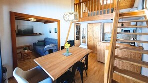 Ein Loft-Zimmer mit Esstisch aus Holz, einer Couch und einer Treppe, die zu einer erhöhten Ebene führt.