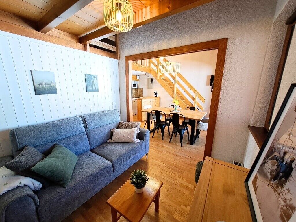 A cozy living room with a sofa, a wooden coffee table, and a staircase leading to a kitchen.