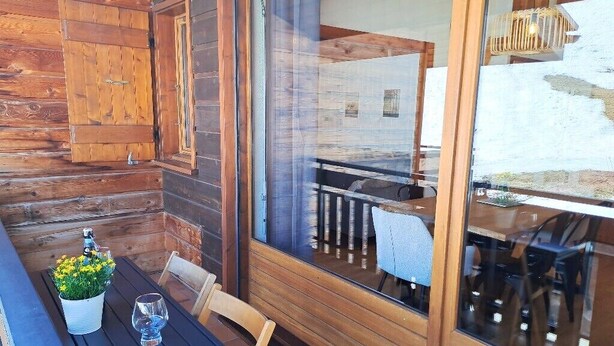 Eine Holzhütte mit Essbereich, inklusive Tisch, Stühlen, einer Zimmerpflanze und einem Glas Wasser.