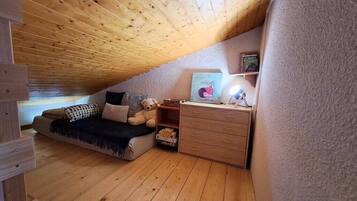 Une chambre mansardée chaleureuse avec un plafond en bois, un lit, une commode et un ours en peluche.