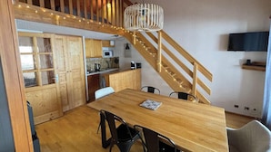 Ein Holzespeisezimmer mit Stühlen, eine Küchenzeile mit Holzschränken, eine Treppe und ein an der Wand befestigter Fernseher.