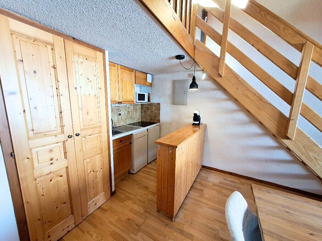 Een kleine keuken met houten kastjes, een inbouwmagnetron en een houten bank.
