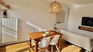 Un comedor con mesa de madera y sillas blancas, una lámpara colgante y un radiador.