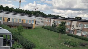 A residential area with a grassy lawn, a patio with outdoor furniture, and a row of apartment buildings in the background. - Room-cozy Guest Room in Green Uppsala - (Uppsala)