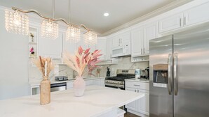 A modern kitchen with white cabinets, a stainless steel refrigerator, a central island with a vase and pampas grass, and pendant lights. - Spacious 3BR/3BA - Sleeps 7 - 10 Min to Stadium (Philadelphia)