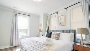 A hotel room with a bed, two bedside tables, a window with curtains, and a wall-mounted artwork. - Spacious 3BR/3BA - Sleeps 7 - 10 Min to Stadium (Philadelphia)