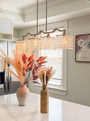 A kitchen with a white countertop, a vase with dried plants, and a chandelier with crystal details.
