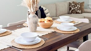 A dining area with a long table set for four, a vase with dried plants, and abstract art on the wall. - Spacious 3BR/3BA - Sleeps 7 - 10 Min to Stadium (Philadelphia)