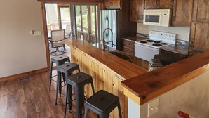 Cozinha com armários de madeira, fogão branco, micro-ondas e banquetas de bar.