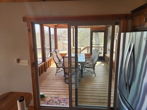 Une terrasse couverte avec une table et des chaises, un réfrigérateur et une vue sur l’extérieur.