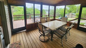 Um deck coberto ao ar livre com mesa e cadeiras, janelas amplas e um ventilador de teto.
