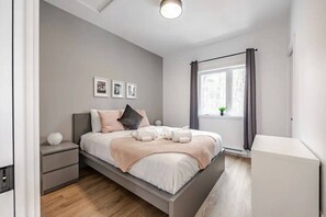 A modern bedroom with a bed, bedside tables, a window with curtains, and a wall-mounted light fixture. - Le Pin | Private Spa & Billiards | Nature & Golf (Brownsburg)