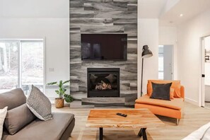 A modern living room with a fireplace, a sofa, a coffee table, and a television mounted on the wall. - Le Pin | Private Spa & Billiards | Nature & Golf (Brownsburg)