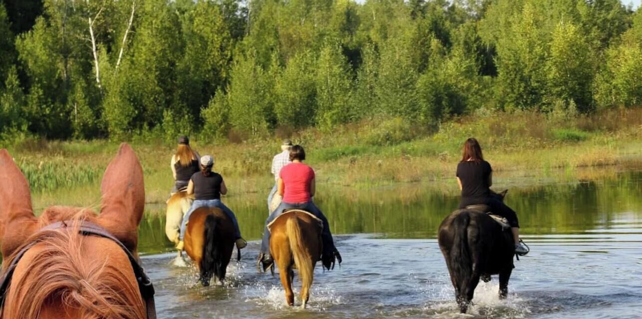 A group of people riding horses along a riverbank.