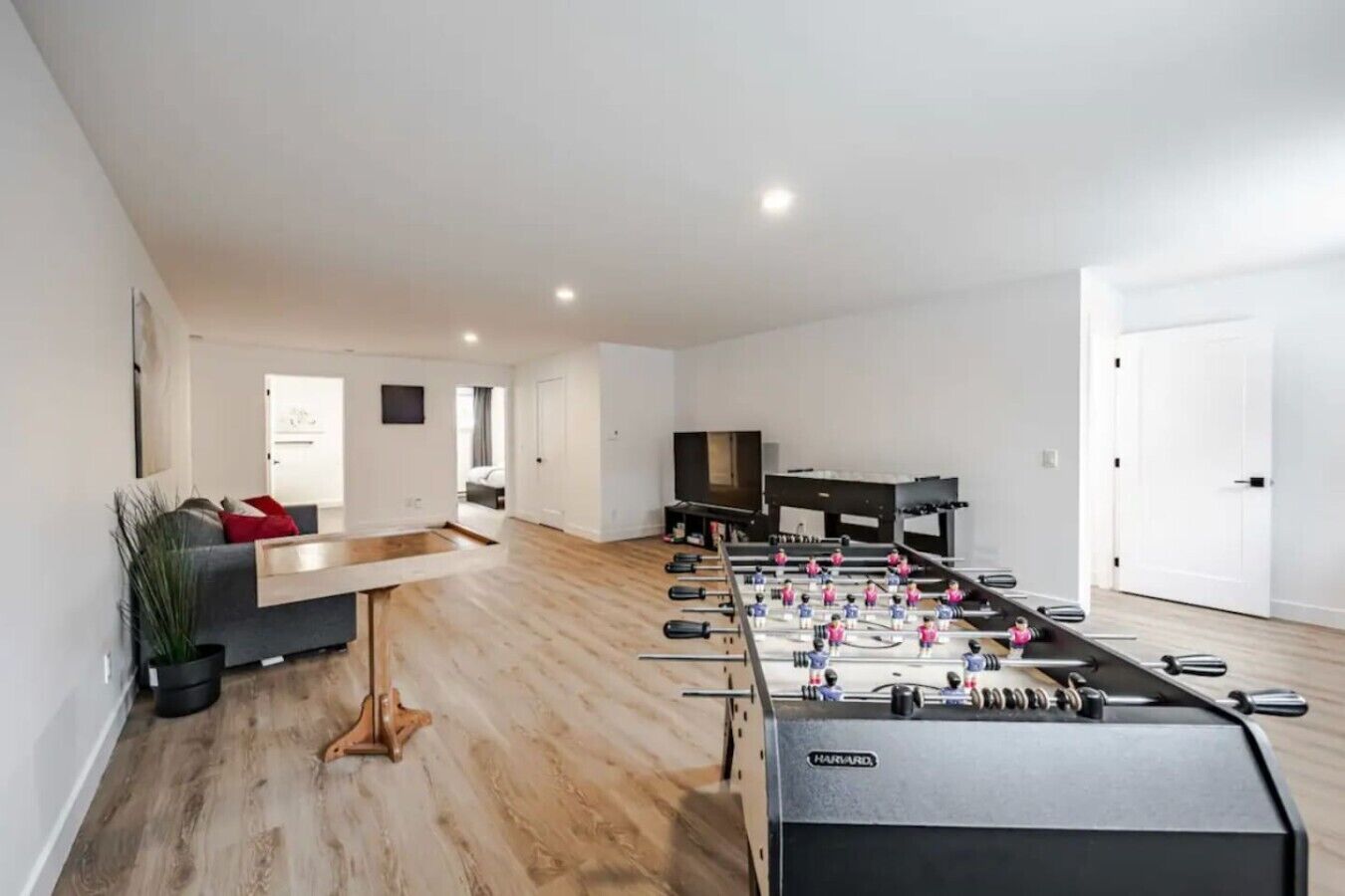 A modern living room with a foosball table, a grey sofa, and a flat-screen TV.
