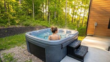 A hot tub in a garden with a wooden house in the background.