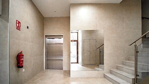 A modern interior with a fire extinguisher mounted on the wall, a door, and a staircase with glass railings. - New Modern Retreat at Malvarrosa Beach (València)