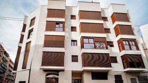 A multi-story building with a modern architectural style, featuring a combination of white and brown facades, large windows, and a prominent entrance. - New Modern Retreat at Malvarrosa Beach (València)