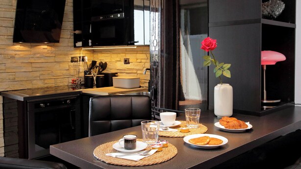 Een moderne keuken met een bakstenen muur, zwarte kastjes en een eethoek met een tafel gedekt voor twee personen.