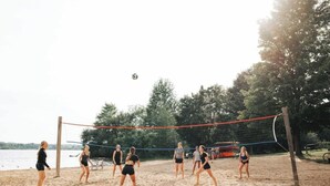 A beach volleyball game with players on a sandy court, surrounded by trees and a body of water. - Écohaven-Spa, nature & feu sous les étoiles (Brownsburg)