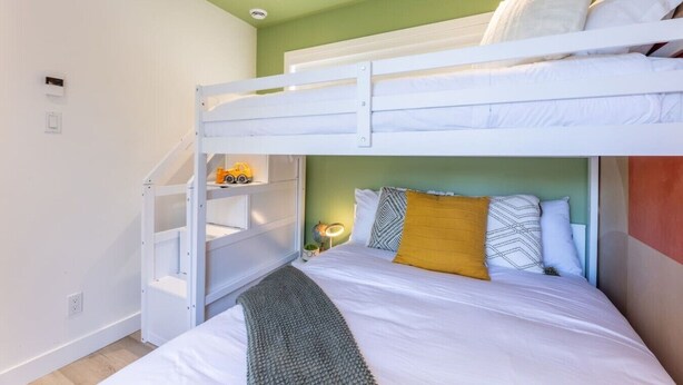 A bunk bed with white bedding, a green wall, and a small shelf with a toy. - Écohaven-Spa, nature & feu sous les étoiles (Brownsburg)
