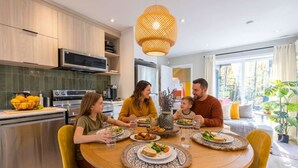 A family dining in a modern kitchen with a round table, yellow chairs, and a large window with a view of trees. - Écohaven-Spa, nature & feu sous les étoiles (Brownsburg)