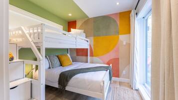 Une chambre avec des lits superposés, un mur décoré d’une fresque abstraite aux couleurs vives, une fenêtre avec des rideaux et un plancher en bois.