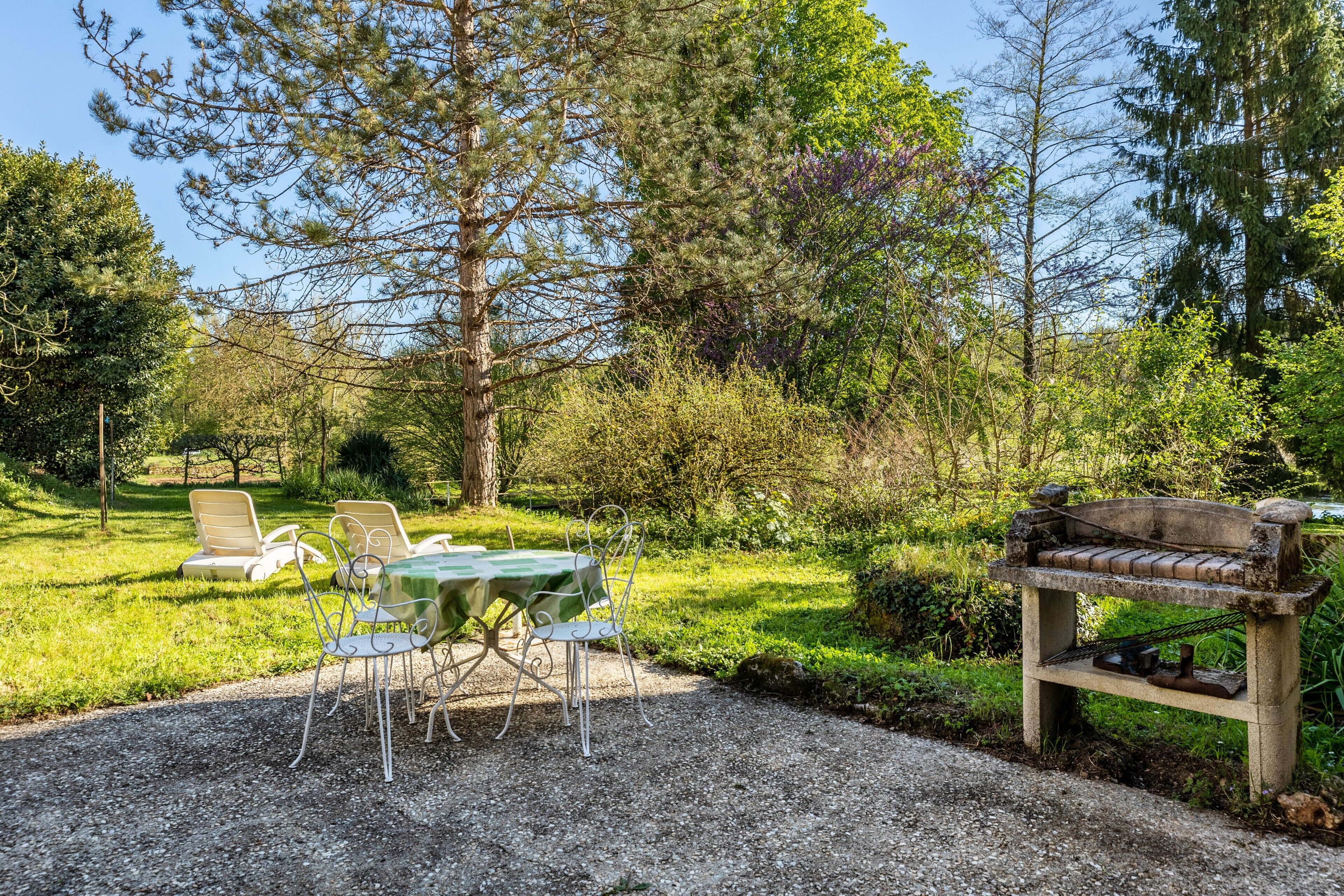Un jardin avec une table et des chaises, un banc et des arbres.