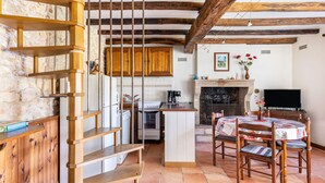 Una cocina rústica con vigas de madera, pared de piedra, escalera de madera, una isla central y un comedor con mesa y sillas.