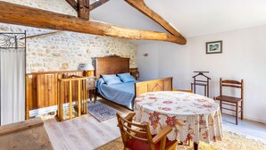 Un dormitorio con una cama, cabecero de madera, una mesa con mantel floral y una silla.