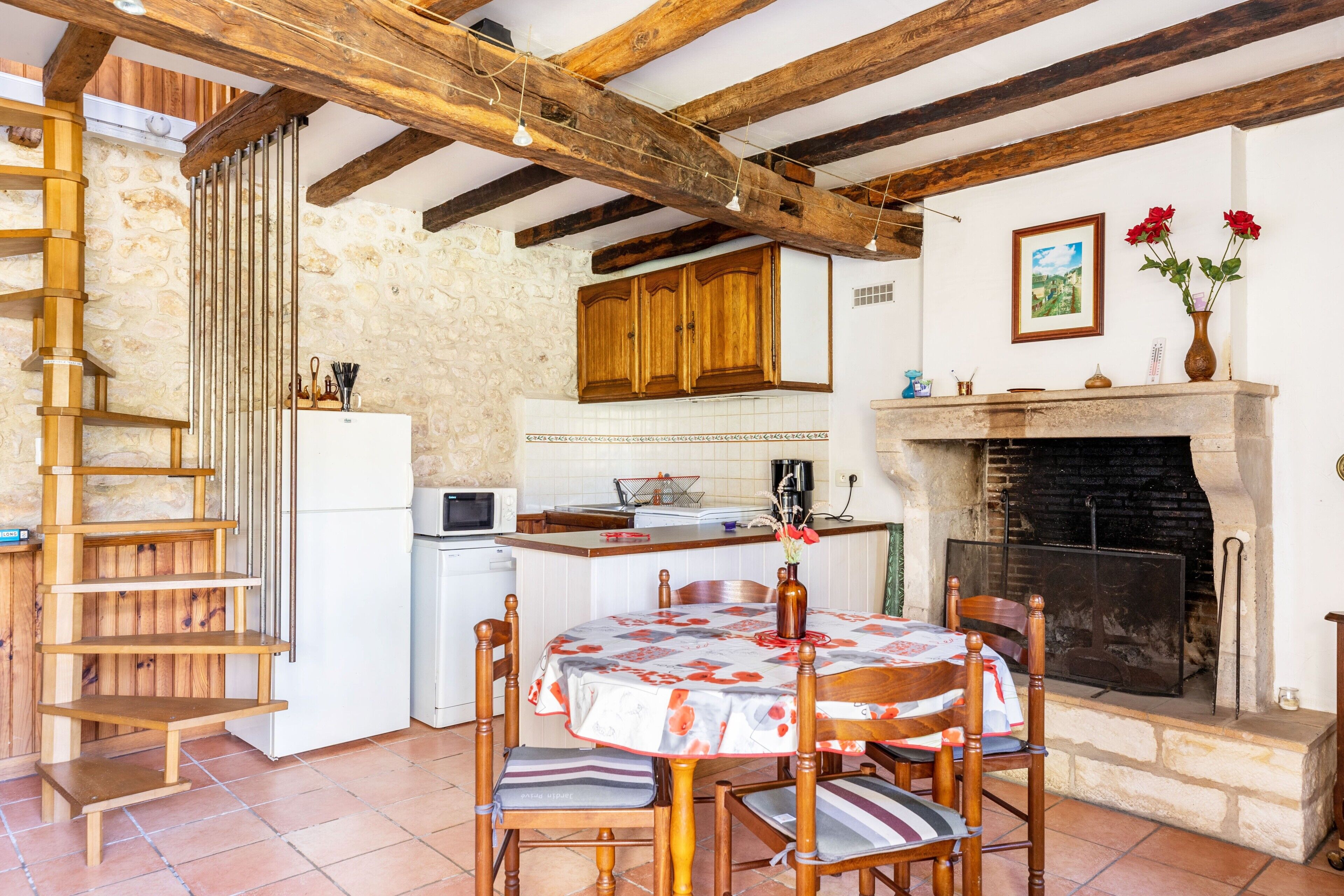Une cuisine rustique avec des poutres en bois, un mur en pierre, un escalier en bois, une table à manger avec des chaises et une cheminée.